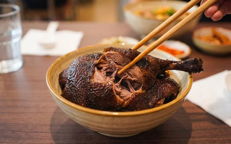 Tender braised duck being carefully pulled apart with chopsticks showing the fall off the bone texture
